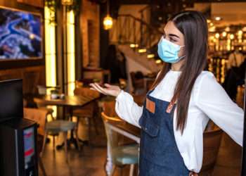 Una camarera abre la puerta de su cafetería // iStock/dragana991